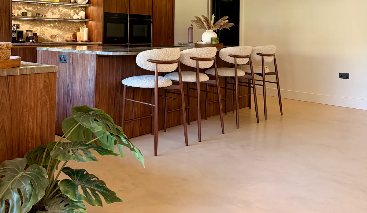 Open-plan kitchen with a timber-fronted island, four bar stools and a pale microcement floor