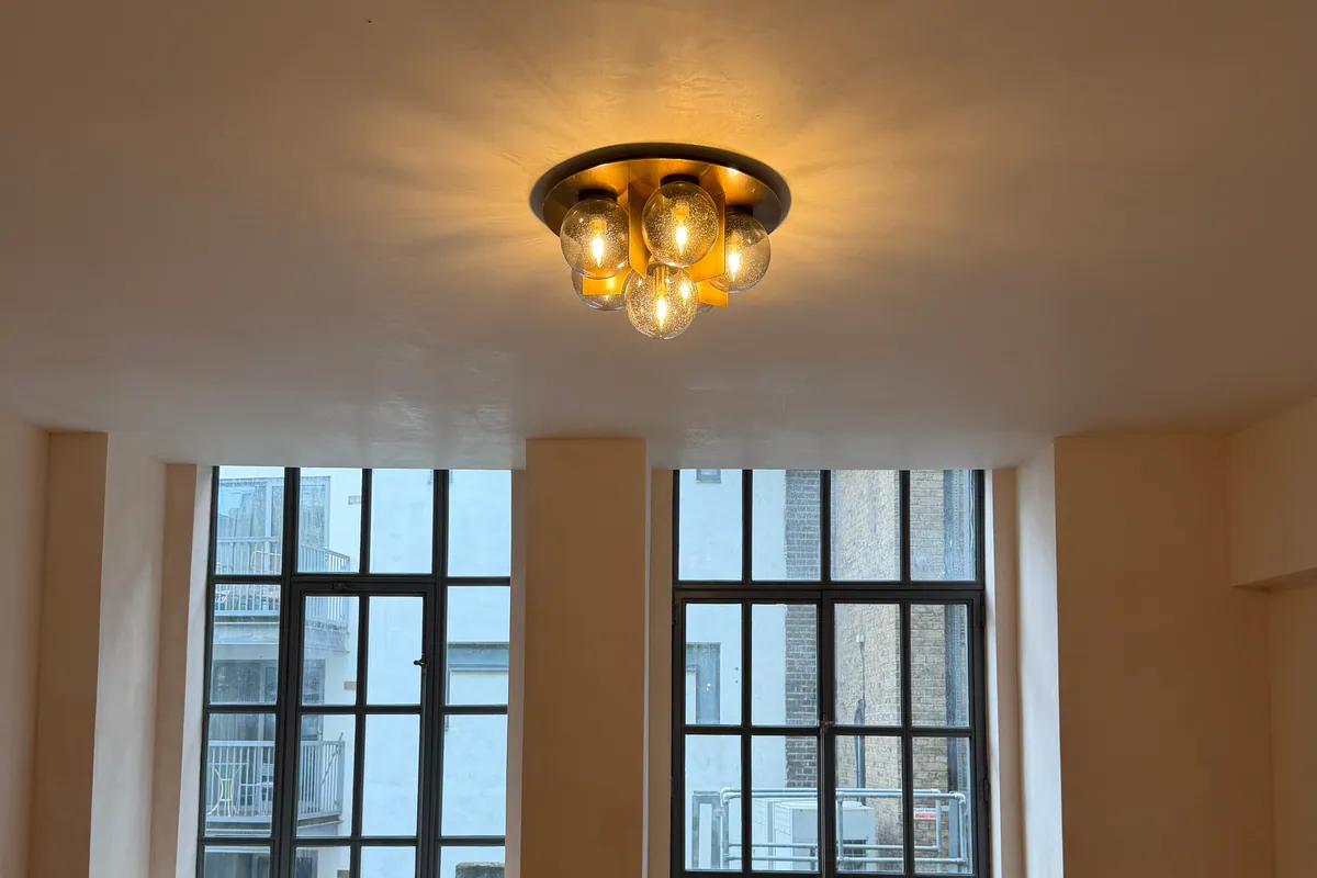 Plastered ceiling with a brass ceiling light above two tall steel-framed windows