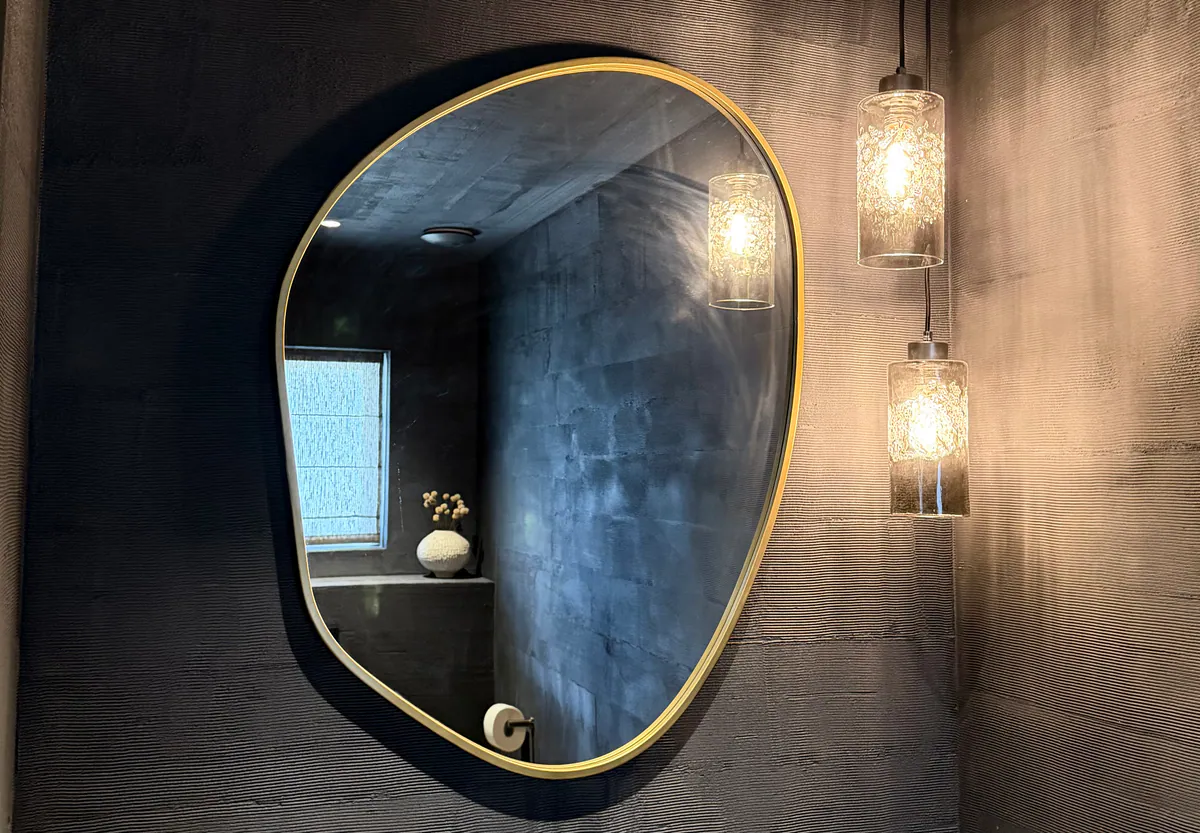 Brass-framed pebble mirror and two glass pendant lights on a charcoal wall with fine horizontal ribbing